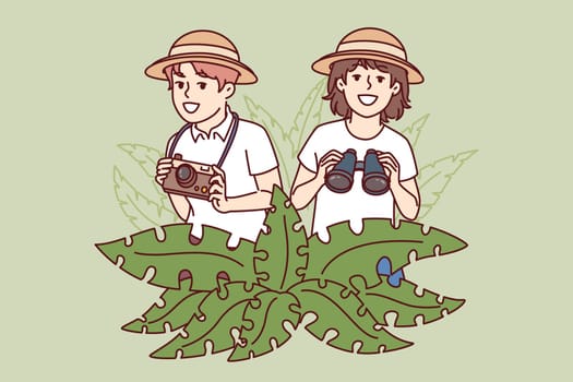 Little travelers stand in jungle with camera and binoculars in hands, spending summer holidays on tropical island. Boy and girl went on trip to exotic jungle, in search of adventure.