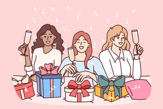 Women celebrate bachelorette party and wish girlfriend happy birthday, drinking champagne and presenting boxes with gifts. Diverse girlfriends posing with smile during fun bachelorette party