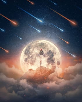 Dreamlike nightscape and a lone man celebrating with balloons in front of the full moon rising above the mountain peak. Inspirational and mysterious background of a starry night with meteor shower