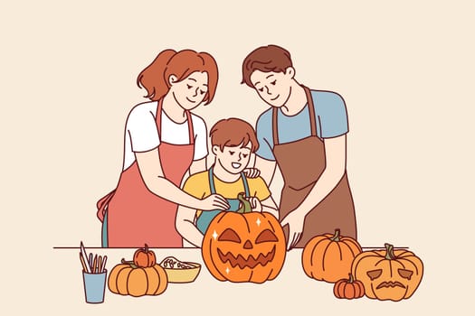 Happy family makes halloween pumpkins to decorate house for october 31st and celebrate all saints day. Boy together with parents, dressed in aprons, cuts out jack-o-lanterns for celebration halloween