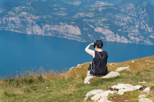 female Holidaymaker on the top of Monte Baldo on Lake Garda near Malcesine takes a photo of the landscape with her smartphone
