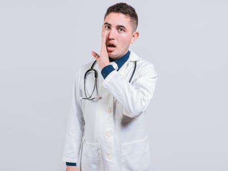Young doctor whispering a secret on isolated background. Handsome doctor telling a gossip isolated,  Doctor telling a secret
