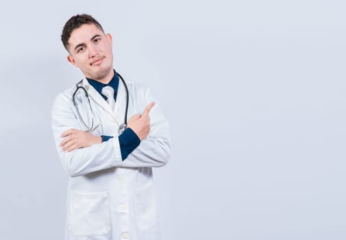 Smiling latin doctor pointing finger at a space isolated. Young doctor showing at a blank space. Doctor pointing at an isolated white space