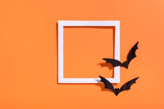 Empty white frame with scary black bats on orange paper. Halloween background layout. Minimal flat lay design.