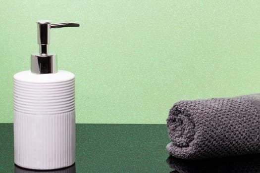 Macro of a beauty cosmetic makeup bottle and a fresh soft terry bath towel on dark table over green glittering background. Copy space for product display montage.