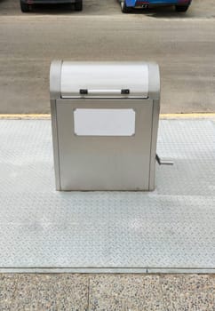 Underground steel dumpster on sideway. Cars parked at an angle on front sideway