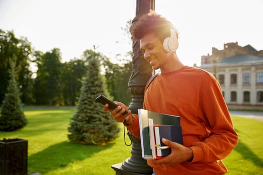 Side view portrait of happy smiling teenager student in wireless headset texting on mobile phone walking outdoors at university campus