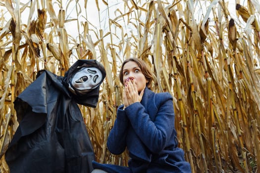 Woman with frightened face near figure with death mask in cornfield on Halloween