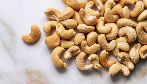 Tasty cashew nuts on a wooden plate on marble table, top view. Space for text