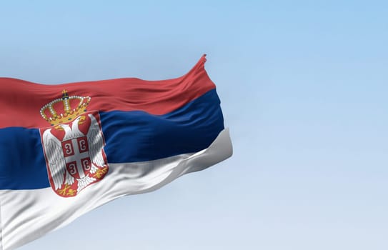 Serbia national flag waving in the wind on a clear day. Red, blue, and white bands, with Serbian coat of arms to the left of the center. 3d illustration render. Fluttering fabric. Selective focus