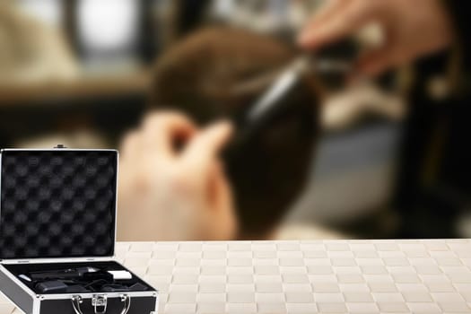 A opened small black silver equipment case or suitcase with professional hairdresser's set over abstract blurred barber shop. Copy space for product display montage.