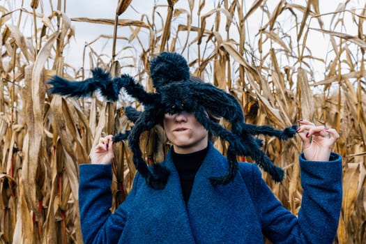 Huge black toy spider on a woman's head in a cornfield during a Halloween party in a cornfield.