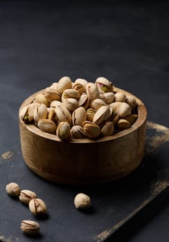 Salted roasted pistachios in a wooden round bowl on the table