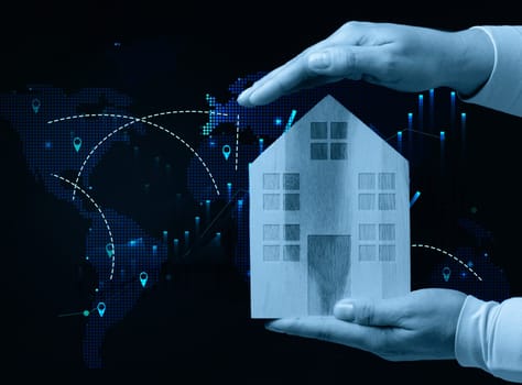 Female hands hold a wooden house against the backdrop of a world map, representing the concept of real estate purchase