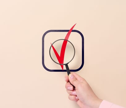 A hand holds a magnifying glass and a sign of approval in a cell. Business approval symbol, yes marks