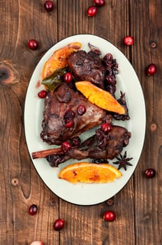 Chicken legs marinated in red wine, baked with orange and berries in white dish. Top view.