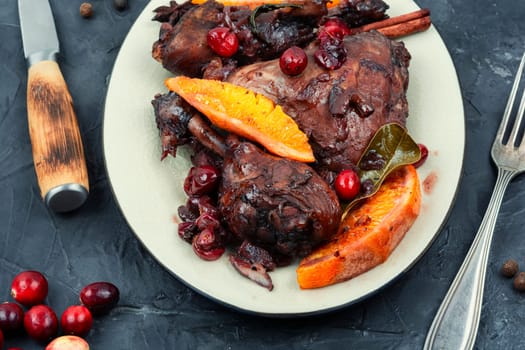 Chicken legs marinated in red wine, baked with orange and berries in white dish. Top view.