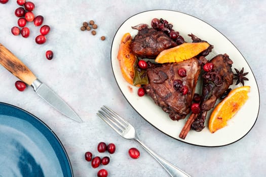 Chicken legs marinated in red wine, baked with orange and berries in white dish. Top view.