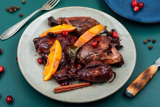 Chicken legs marinated in red wine, baked with orange and berries in white dish. Top view.