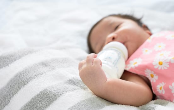Hand of newborn baby 1 month old holding plastic milk bottle. Infant girl lying alone in bed and drinking milk from bottle. Healthy infant nutrition concept