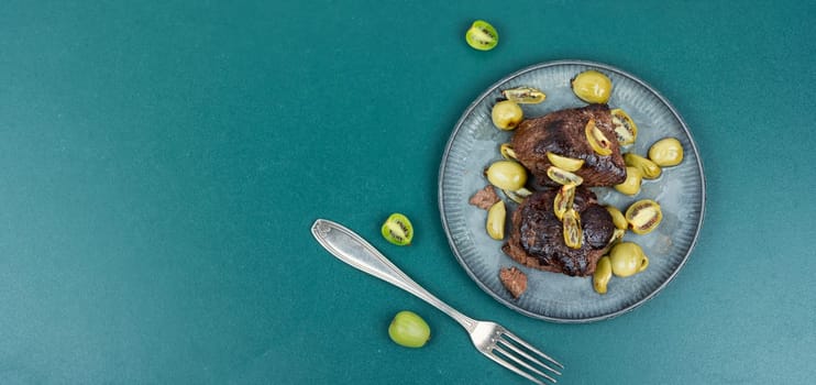 Dish of ostrich steak roasted with mini kiwi sauce. Meat with kiwi berries on wooden table.