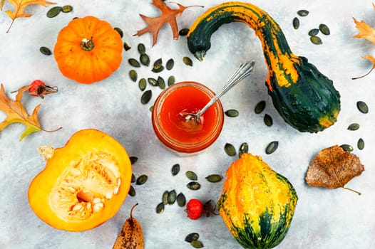 Autumn sweet pumpkin jam in a glass jar and fresh pumpkins. Pumpkin confiture.