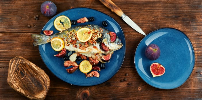 Baked gilt head bream, dorado fish with almonds and figs on rural wooden table. Autumn recipe.