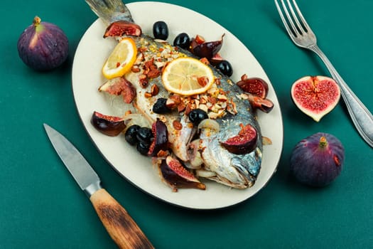 Baked gilt head bream, dorado fish with almonds and figs on rural wooden table. Autumn recipe.