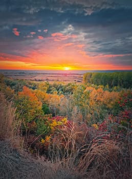Silent autumn evening over the valley. Multicolored fall forest and orange october sunset
