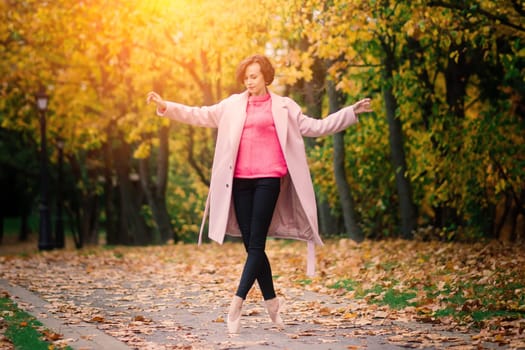 Ballerina dancing in nature among autumn leaves in fair coat.