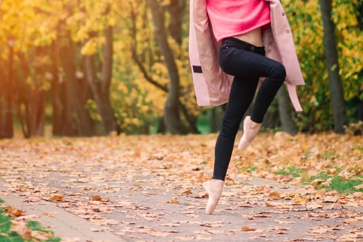 Woman ballerina dancing in pointe shoes in golden autumn park, standing in ballet pose on yellow leaves
