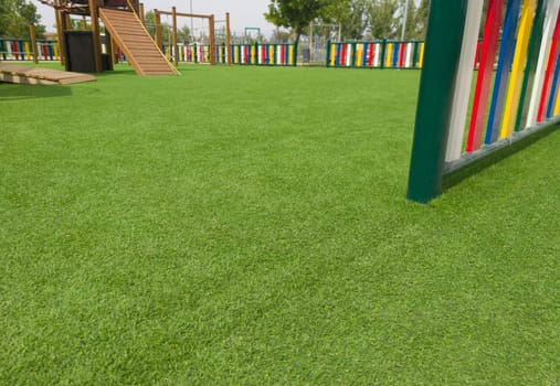 Artificial green grass floor on playground. Colourful rows of painted posts arround