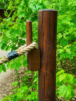 Close-up view of a small waist-high pillar with wooden hooks and hemp rope attached.
