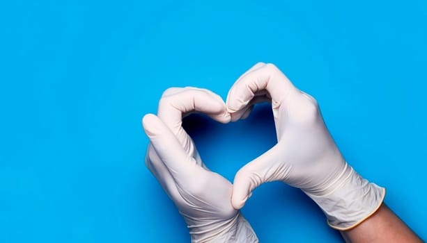 Doctor's hands in medical gloves in shape of heart on blue background with copy space.