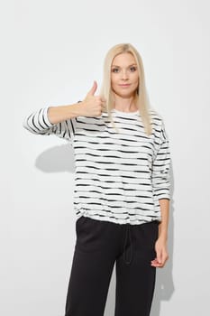 Blonde woman shows thumb up gesture in bright studio