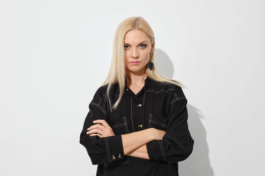 Incredulous woman stands with her arms crossed against white wall