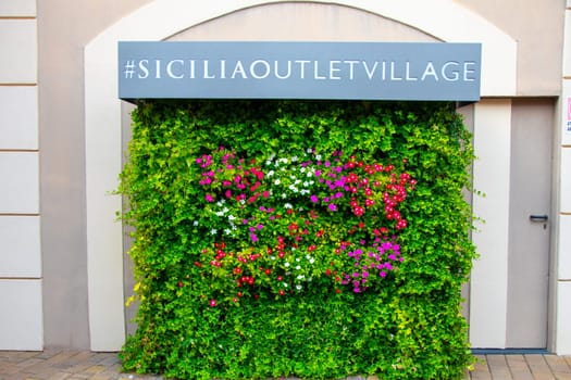 AGIRA, SICILY, Italy - 30 SEP 2023. Sicilia Outlet Village shopping centre is a popular visitor magnet for holidaymakers and locals alike. Flower advertisement wall.