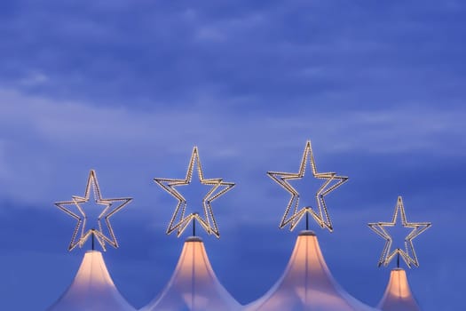 Wonderful x-mas season scene for visual or greetings card. Beautiful market tents with magic orange stars and blue sky at evening time.