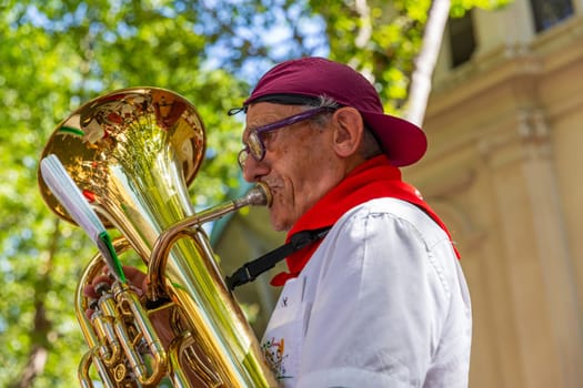 Pamplona, Spain: 09 July 2023: Man playing trombone to celebrate San Fermin festival in traditional white abd red clothing with red necktie, Pamplona, Navarra, Spain.
