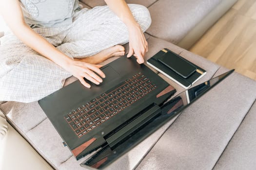 A woman uses a laptop touchpad sitting at home on the couch.