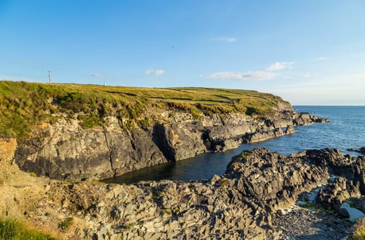 Green hills on the Atlantic Ocean on a sunny spring day. Blue sky over the sea coast. The coastline of Ireland, West Cork.