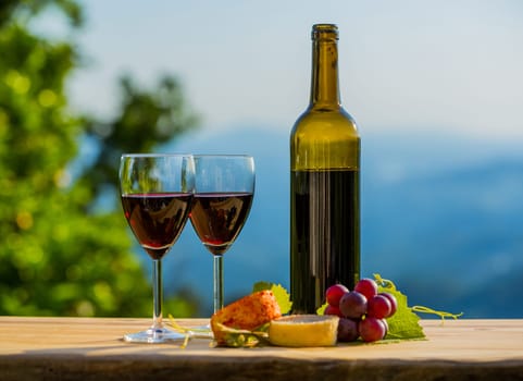 wine bottle, grapes, cheese and bread, on wooden table, outdoor