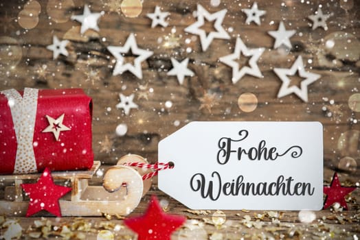 Wooden Sled With Red Gift And Rustic Snowy Christmas Background With Label With German Text Frohe Weihnachten, Which Means Merry Christmas In English