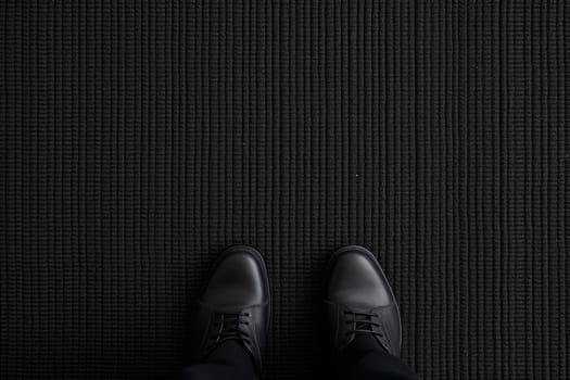 male feet in shoes stand on a black carpet, top view. copy space.Generative AI