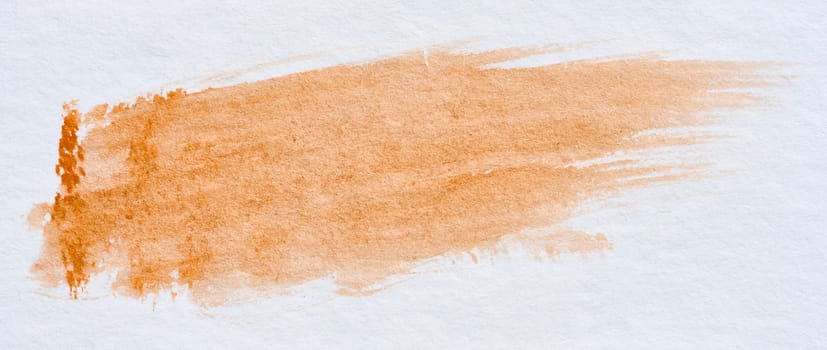 A stroke of orange watercolor paint on a white sheet of paper