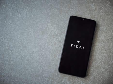 Lod, Israel - July 16,2023: TIDAL Music app launch screen on smartphone on ceramic stone background. Top view flat lay with copy space.