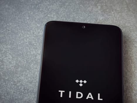 Lod, Israel - July 16,2023: TIDAL Music app launch screen on smartphone on ceramic stone background. Top view flat lay with copy space.