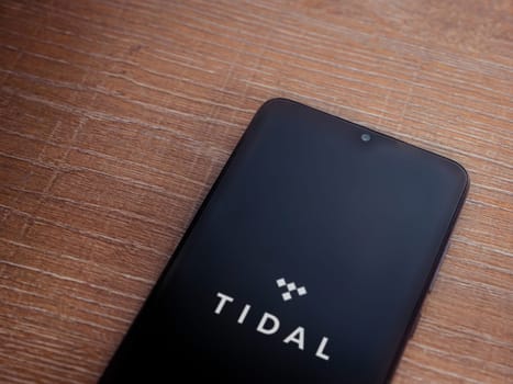 Lod, Israel - July 16,2023: TIDAL Music app launch screen on smartphone on wooden background. Top view flat lay with copy space.