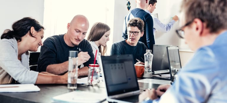 Startup business and entrepreneurship problem solving. Young AI programmers and IT software developers team brainstorming and programming on desktop computer in startup company share office space
