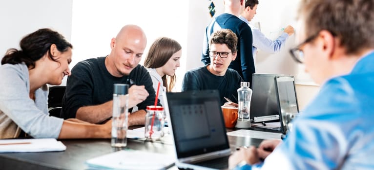 Startup business and entrepreneurship problem solving. Young AI programmers and IT software developers team brainstorming and programming on desktop computer in startup company share office space